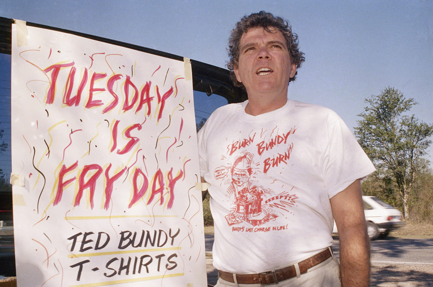 Na foto: Um dia antes da execução de Ted Bundy, homem vende camisetas com a inscrição "Frite Bundy Frite" nos arredores da Prisão Estadual da Flórida. Créditos: Spiegel.