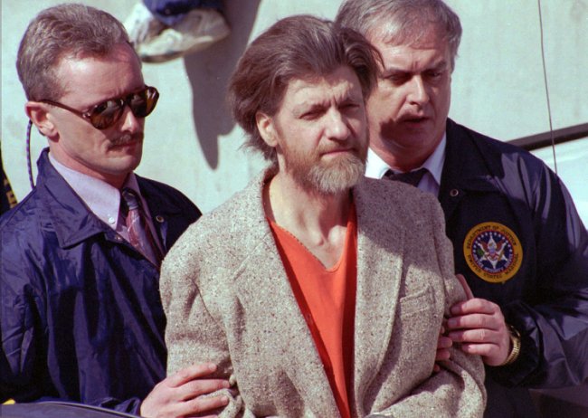 Theodore John Kaczynski, escoltado por oficiais federais enquanto é levado de um tribunal federal em Helena, Montana, em 4 de abril de 1996, quinta-feira. Kaczynski, suspeito de ser o Unabomber, foi indiciado em uma acusação de possuir componentes para uma bomba (AP Photo/John Youngbear).